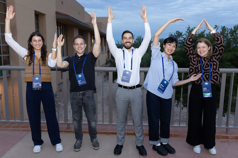 Five people with arms raised in shapes that spell out W-U-C-A. 